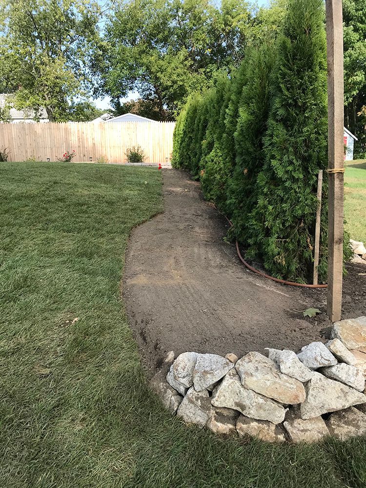 A stone wall surrounds a path in a backyard.