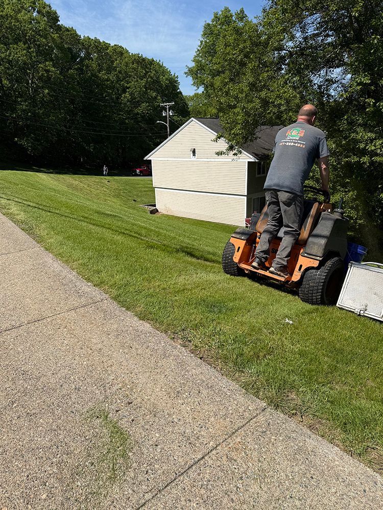 A man is riding a lawn mower down a sidewalk.