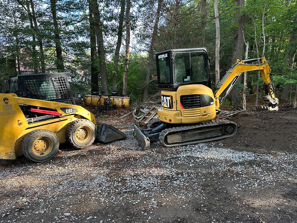 A yellow excavator is sitting next to a yellow skid steer loader in a dirt lot.