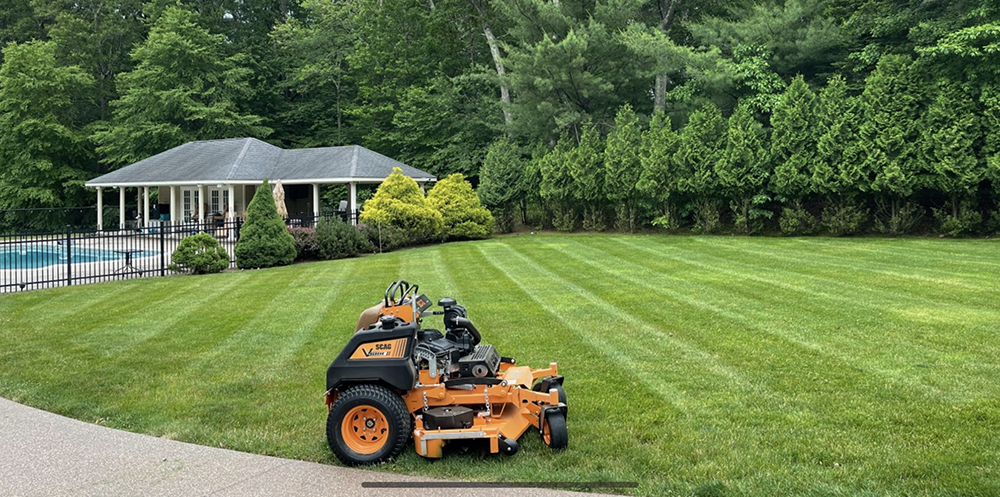 A lawn mower is sitting on the side of a lush green lawn in front of a house.