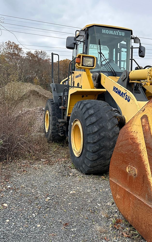A yellow bulldozer is parked on a gravel road next to a rusty bucket.