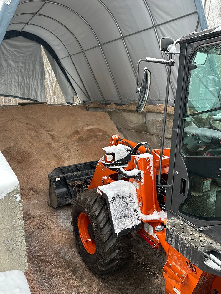 An orange tractor is parked in front of a large pile of snow.