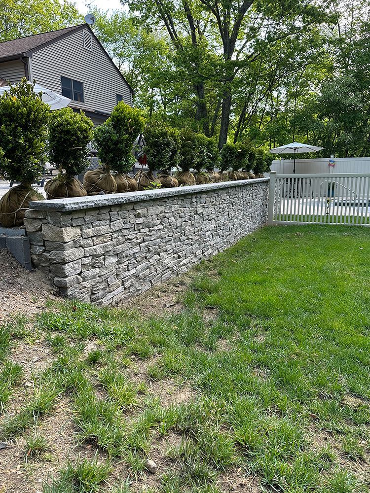 A stone wall surrounds a lush green lawn in front of a house.