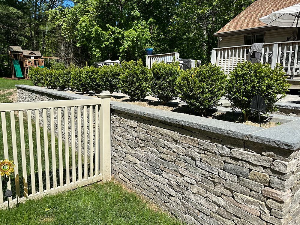A stone wall with a white fence in front of a house.