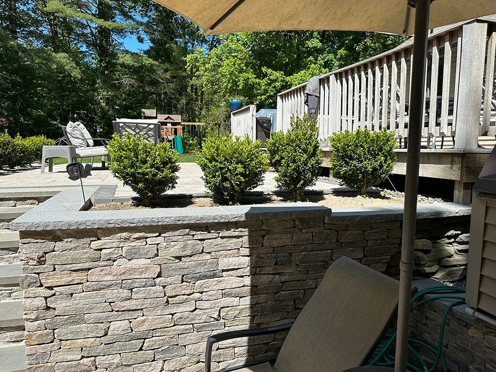 A patio with a chair and umbrella and a stone wall