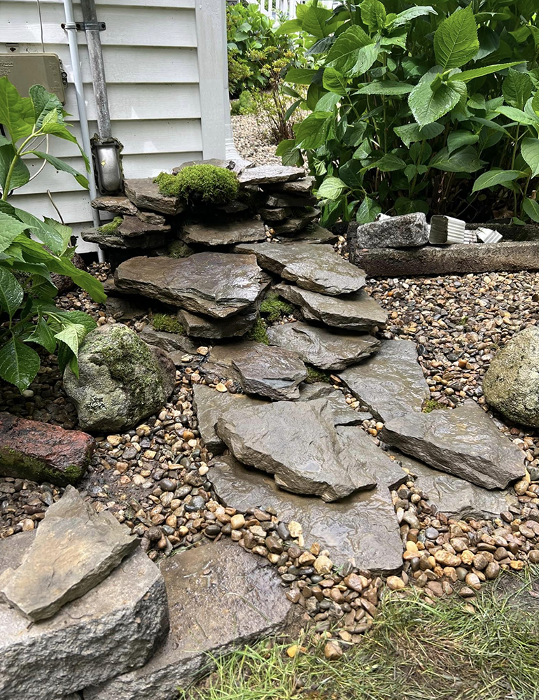 A stone walkway in a garden next to a house.