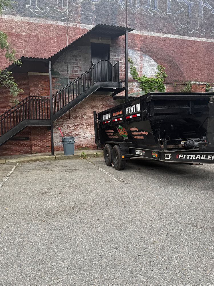 A dumpster is parked in front of a brick building with stairs.
