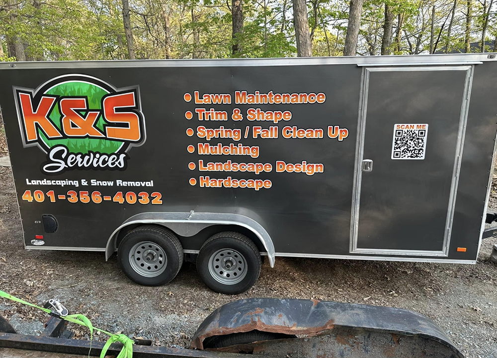 A trailer for k & s services is parked in the woods