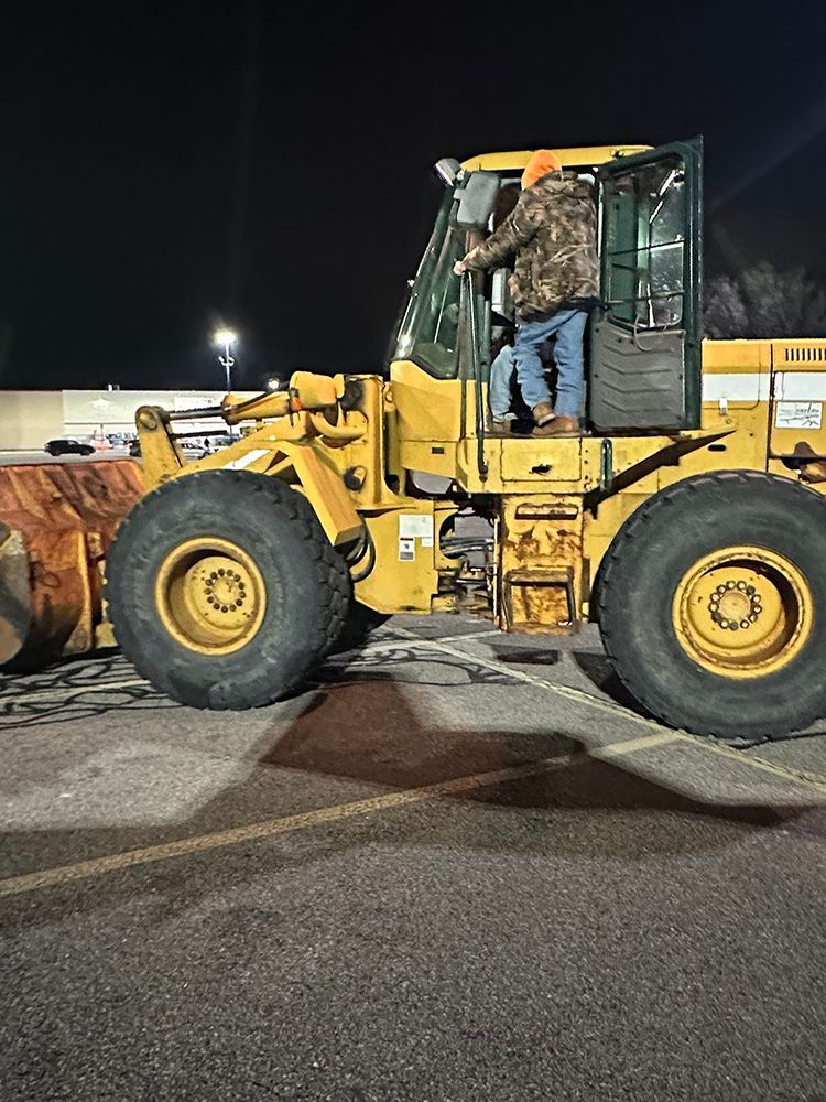 A man is sitting on a yellow tractor in a parking lot at night.