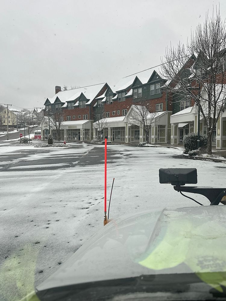 A car is driving down a snowy street with a red pole in the foreground.