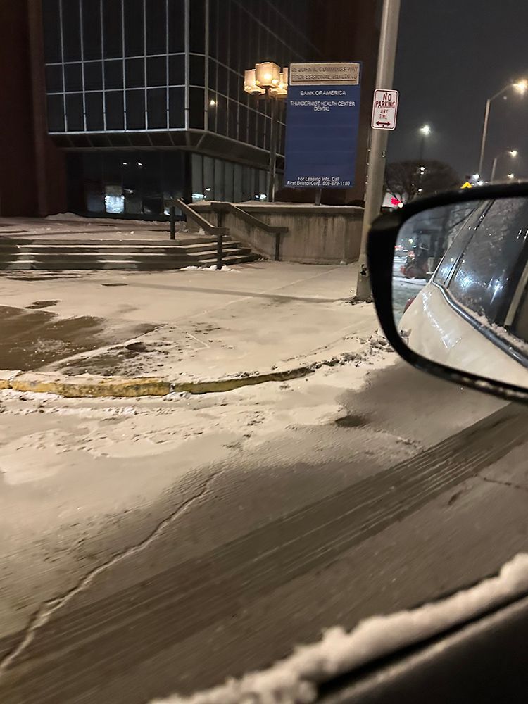 A car is driving down a snowy street at night.