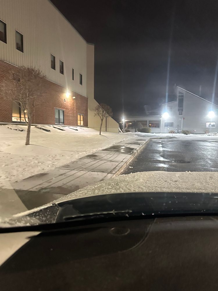 A car is driving down a snowy street at night.
