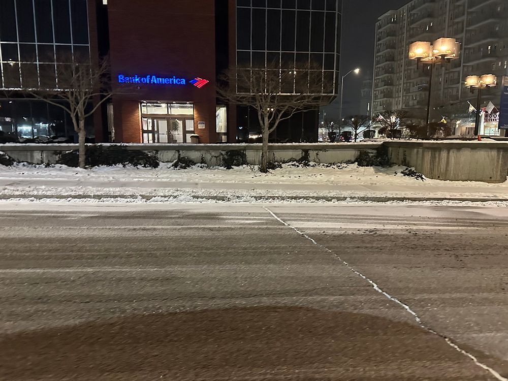 A snowy street with a bank of america building in the background