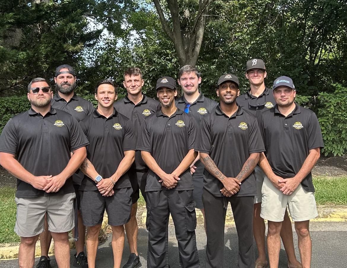 Group of men in black shirts and khaki/black shorts, posing outdoors.