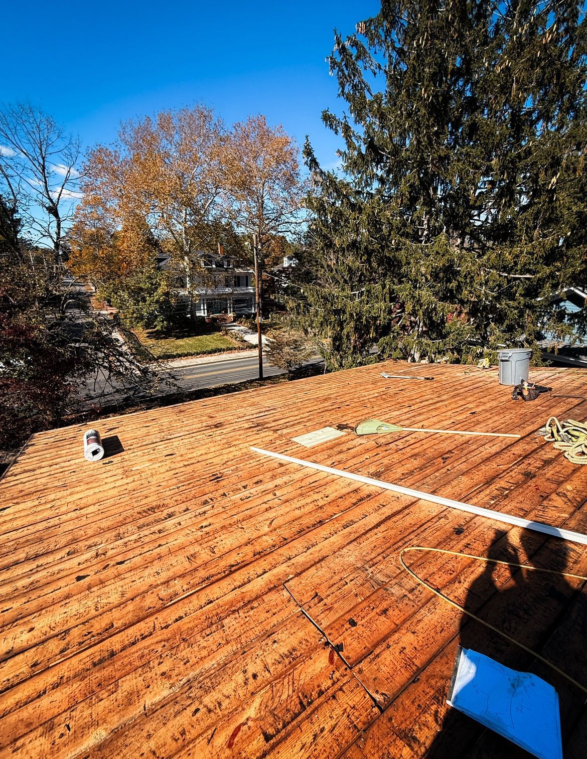 Brown roof with various pipes and lines, surrounded by trees and a neighborhood view.