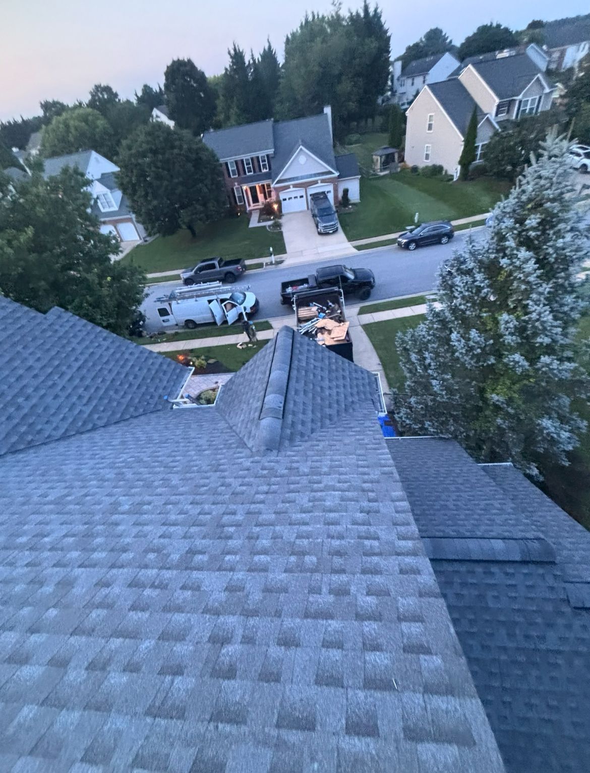 Gray shingled roof, aerial view of a suburban neighborhood street with houses, vehicles, and trees.