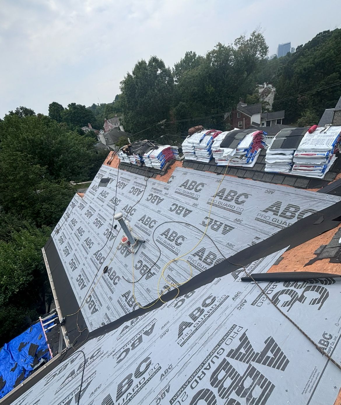 Roof partially covered in protective underlayment; stacks of new shingles; residential setting.