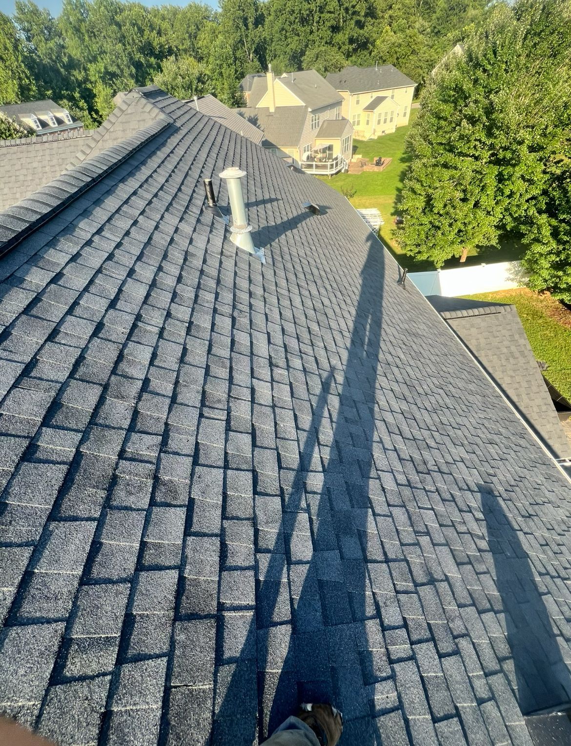 Dark gray shingle roof of a house with a vent pipe, sunny day.