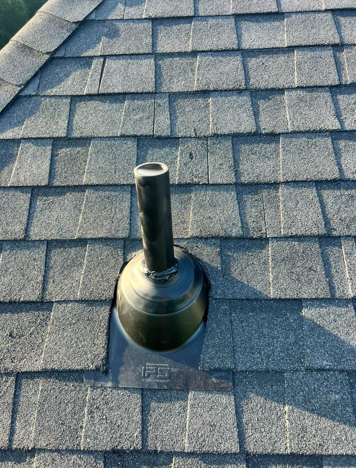 Black plumbing vent pipe protruding from asphalt shingle roof.