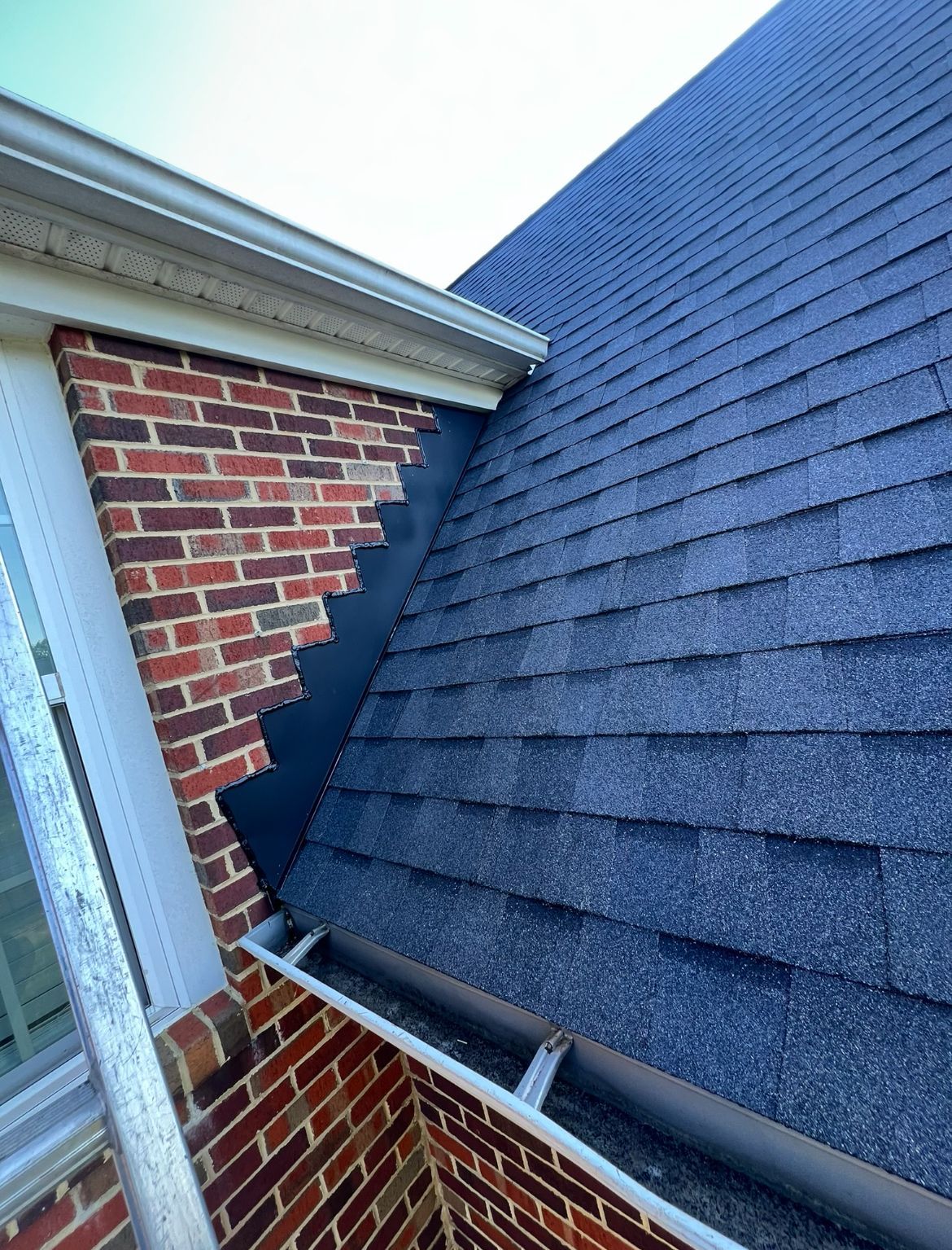 Brick wall angled next to a dark blue shingled roof with a gutter.