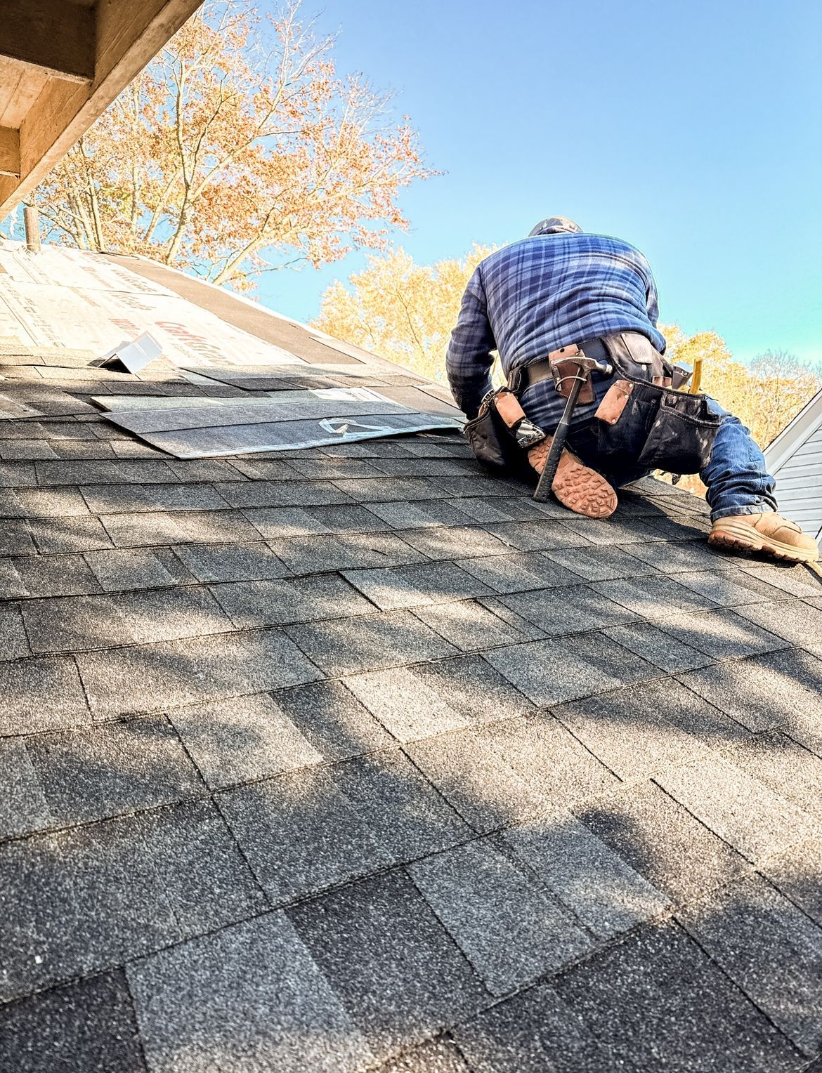 Roofer repairing asphalt shingles on a sunny day.