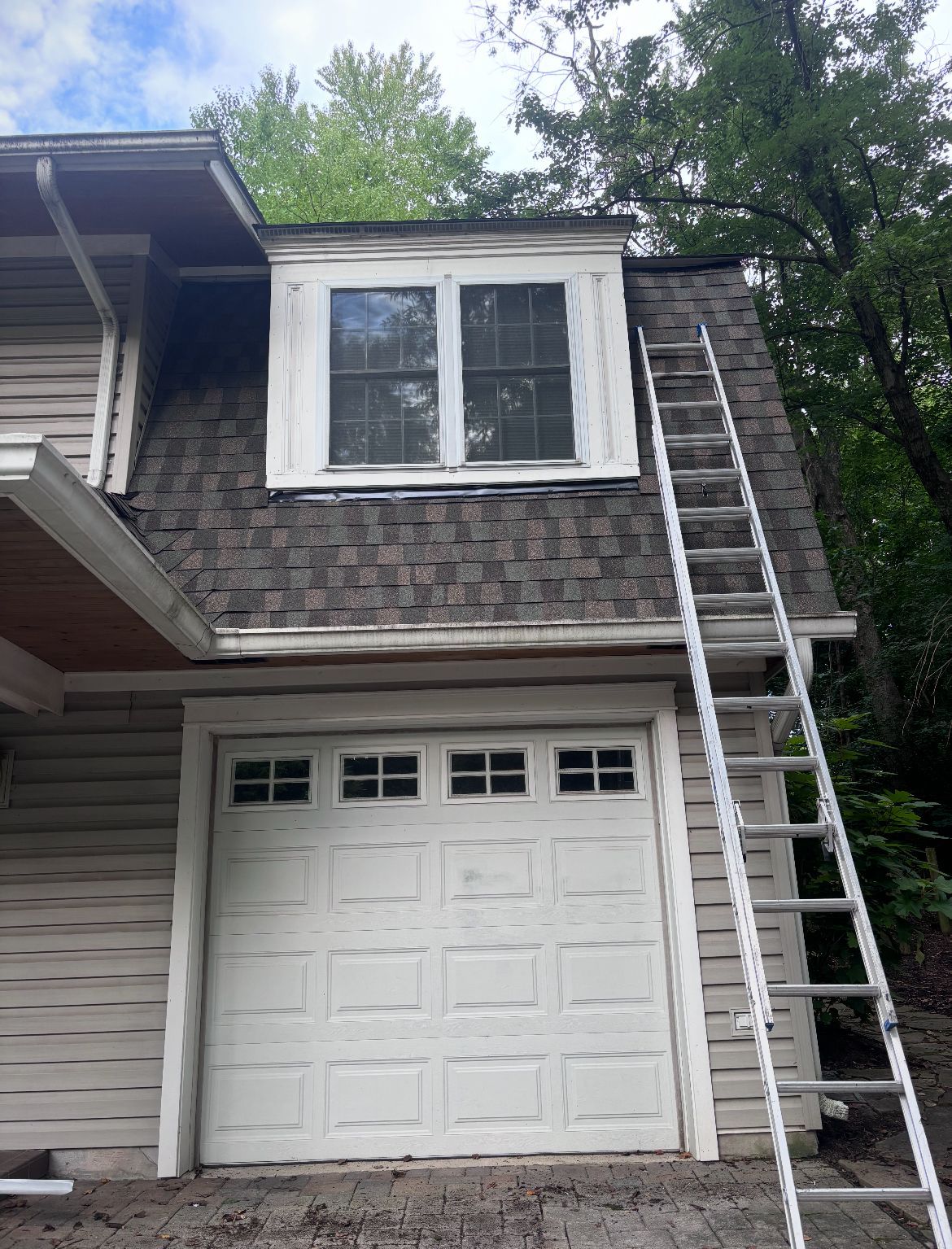 Garage with a white door, brown roof, and a ladder leaning against the side.