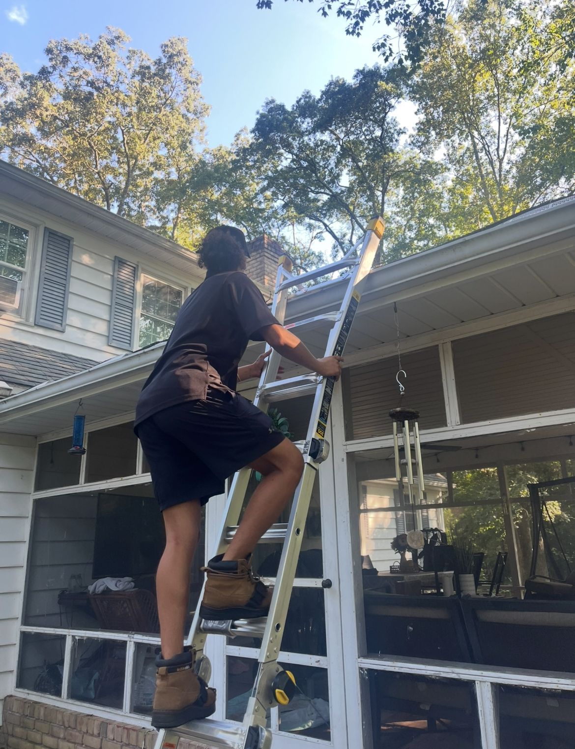 Person on a ladder cleaning a gutter on a house. Outdoors, sunny day.