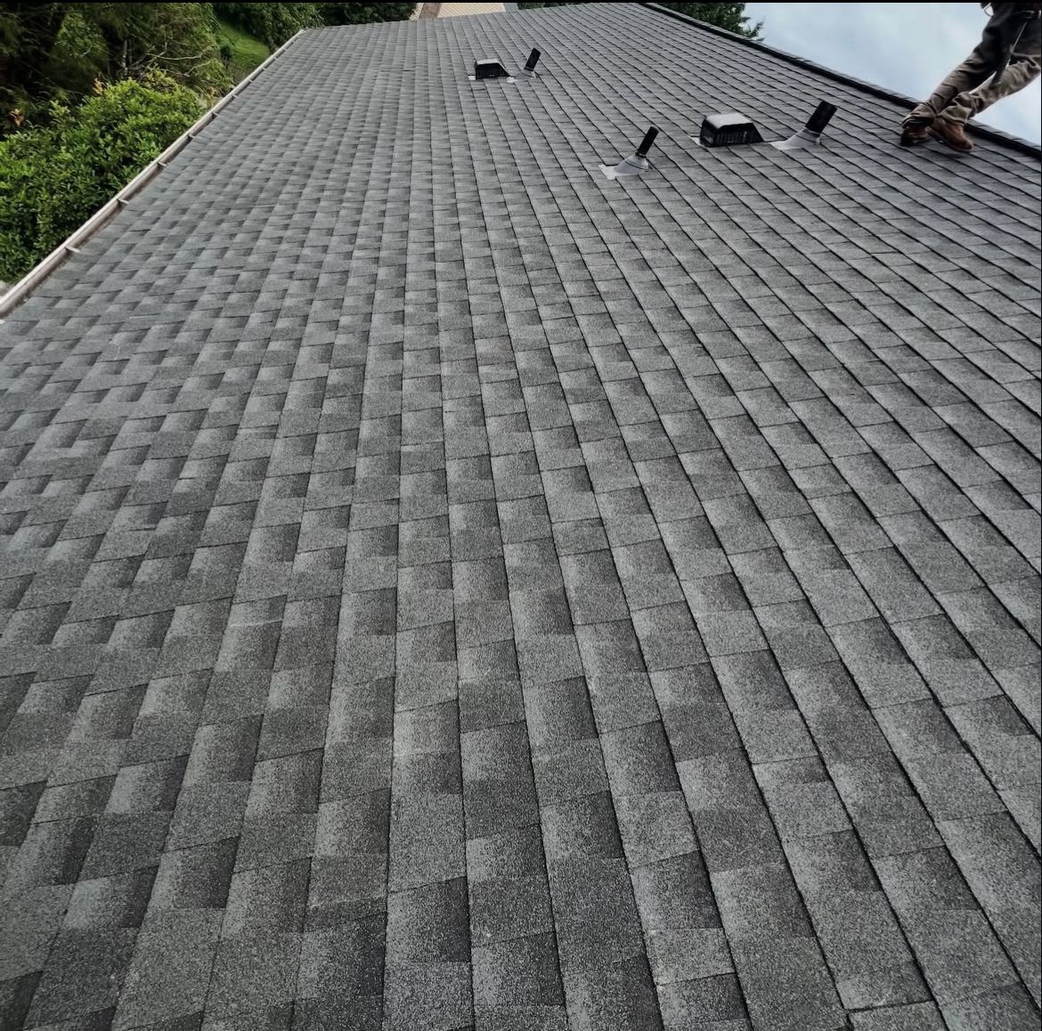 Dark gray asphalt shingle roof, angled view. A person works at the upper right.