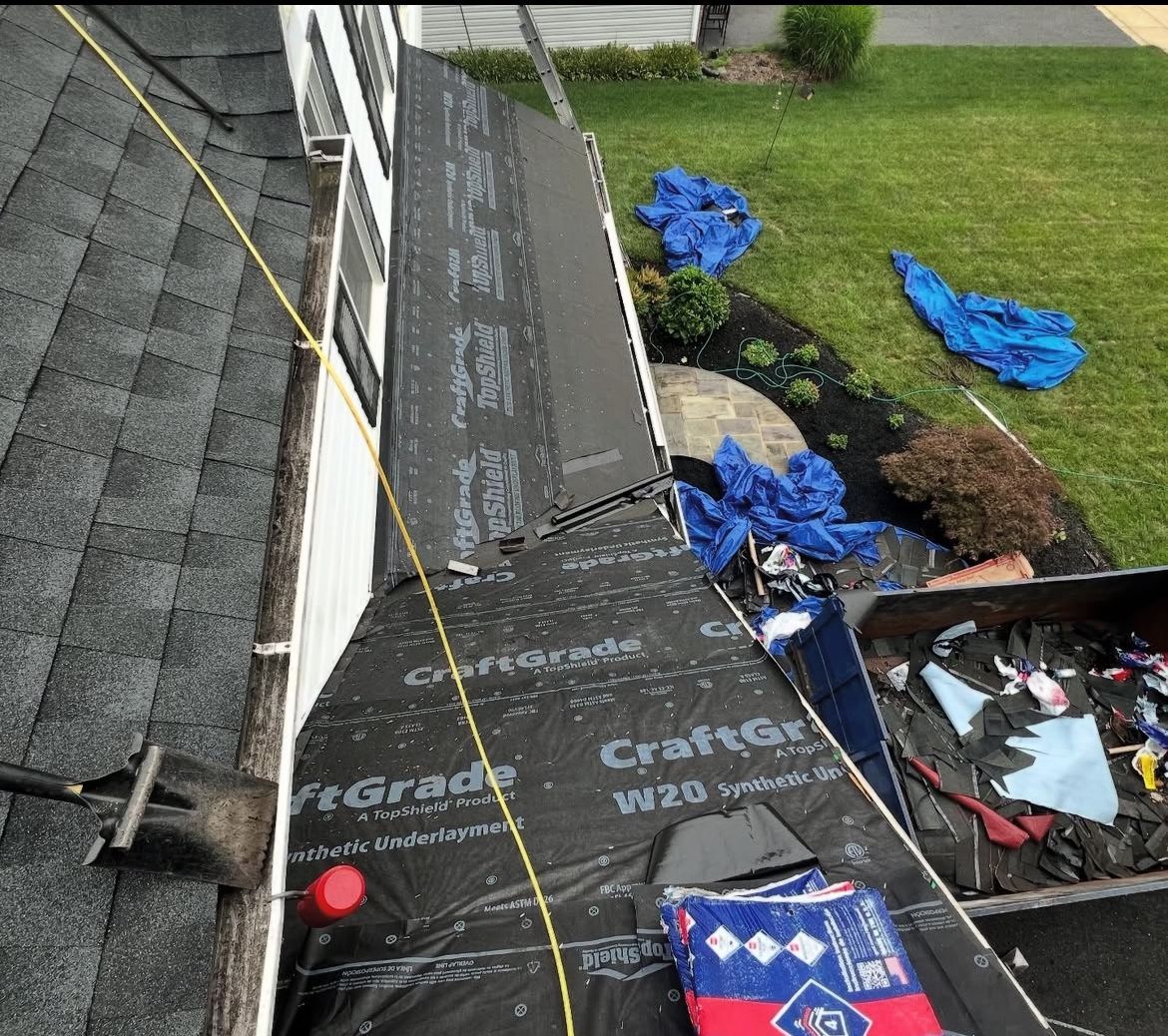 Roof under construction, dark shingles, black underlayment, and debris on the ground.