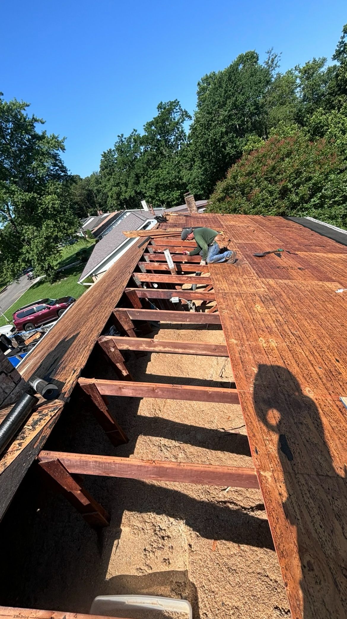 Roof partially demolished, revealing wooden structure and debris under a clear blue sky.