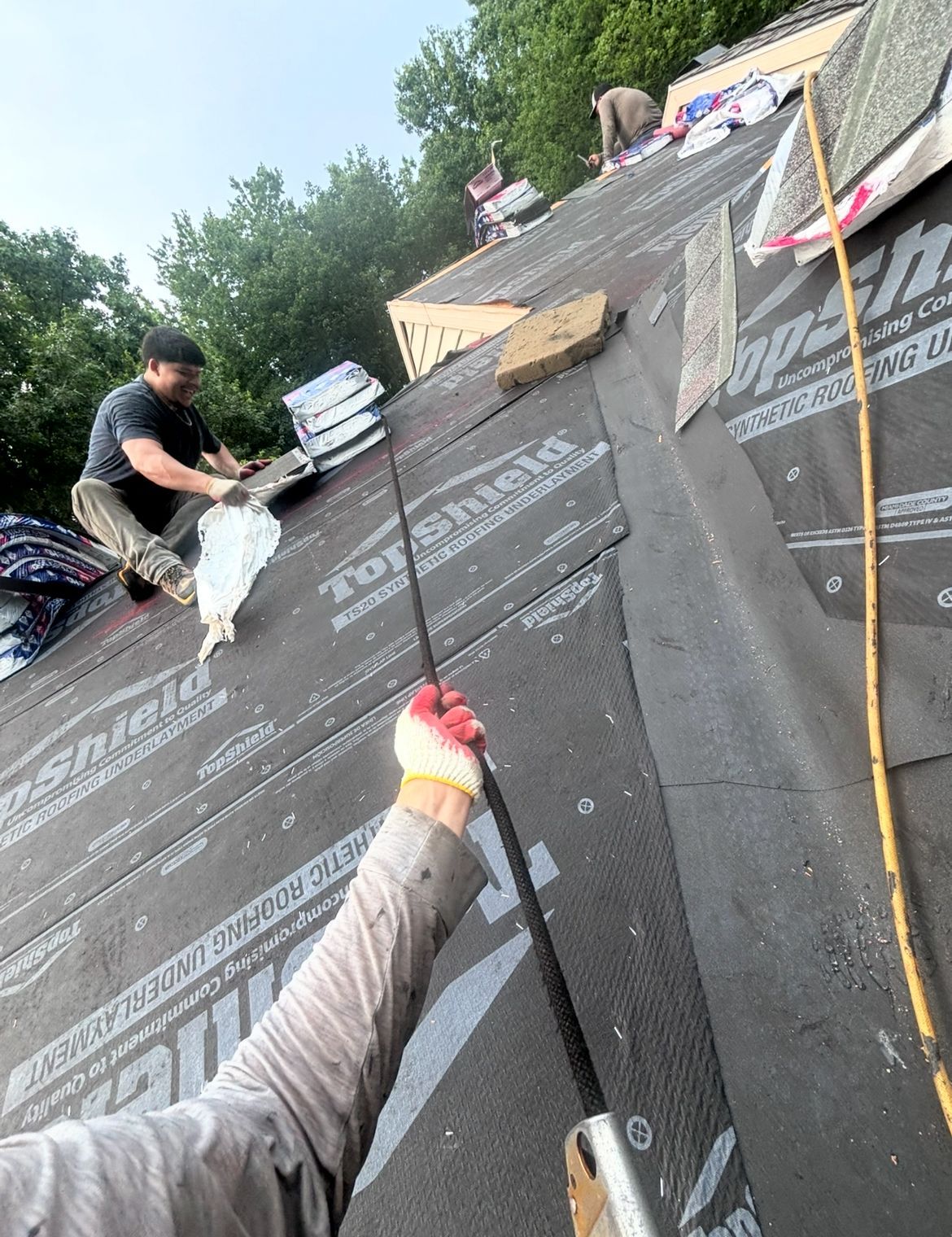 Roofers installing shingles on a house roof, with black underlayment.