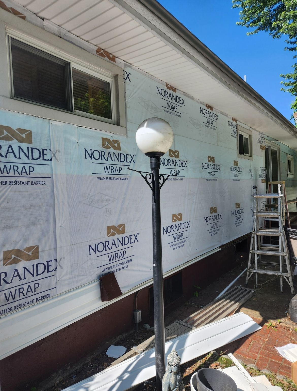 House with sheathing and tarpaper. A black light post stands in front. A ladder rests by a door.