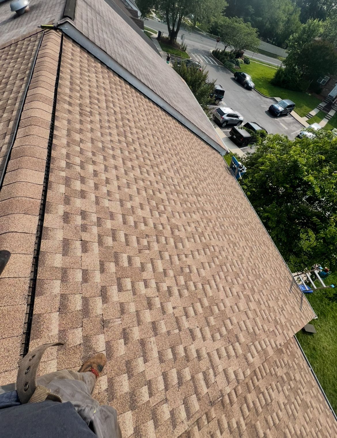 View from above of a brown shingle roof on a house, with a street and trees visible in the background.