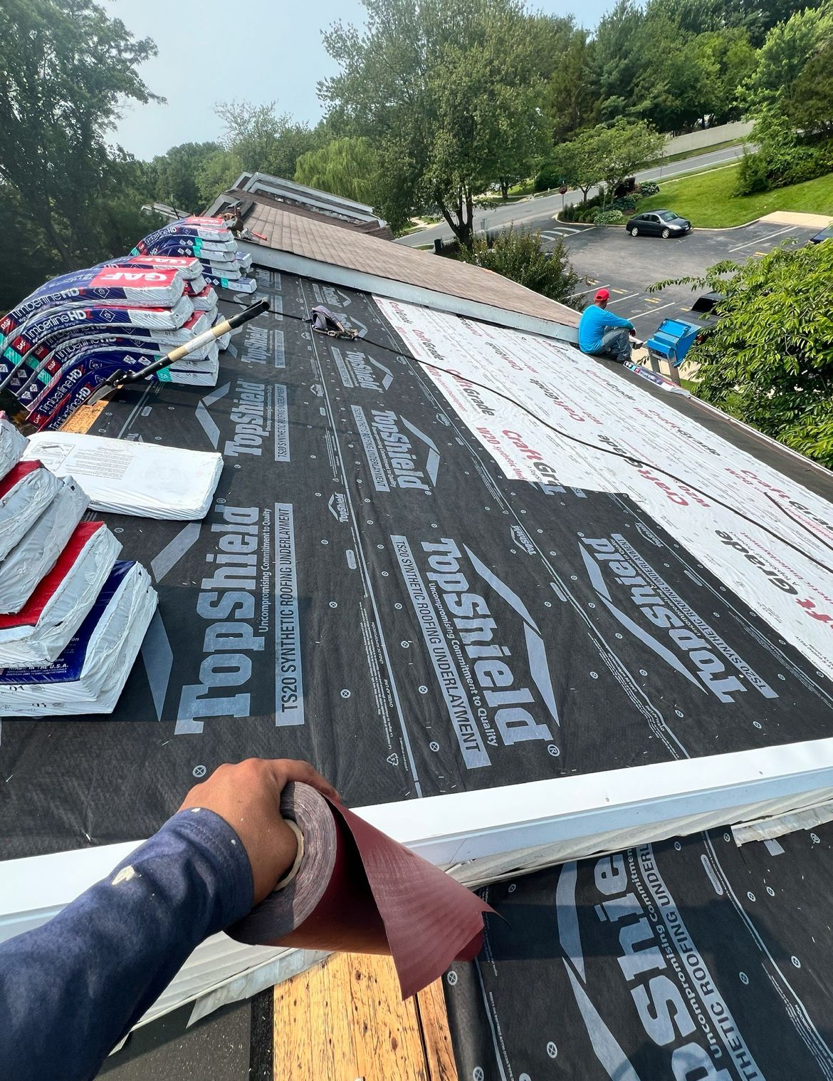 Roofers installing new shingles. Black underlayment visible, materials and workers on the roof.