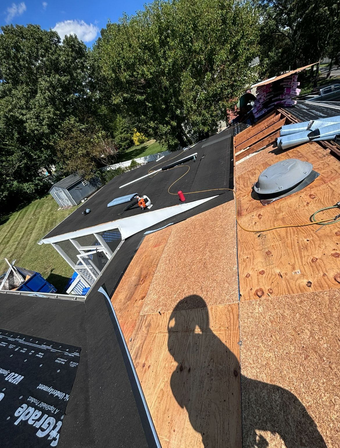 Roofer working on a roof, sunny day. The roof is partially covered with new black roofing material.