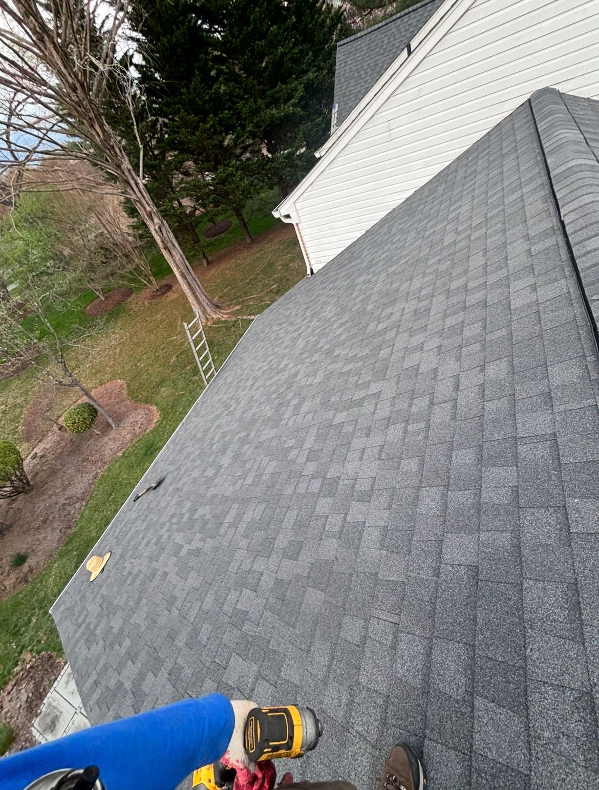 Roof with gray shingles, viewed from above, with a blue and yellow tool visible.