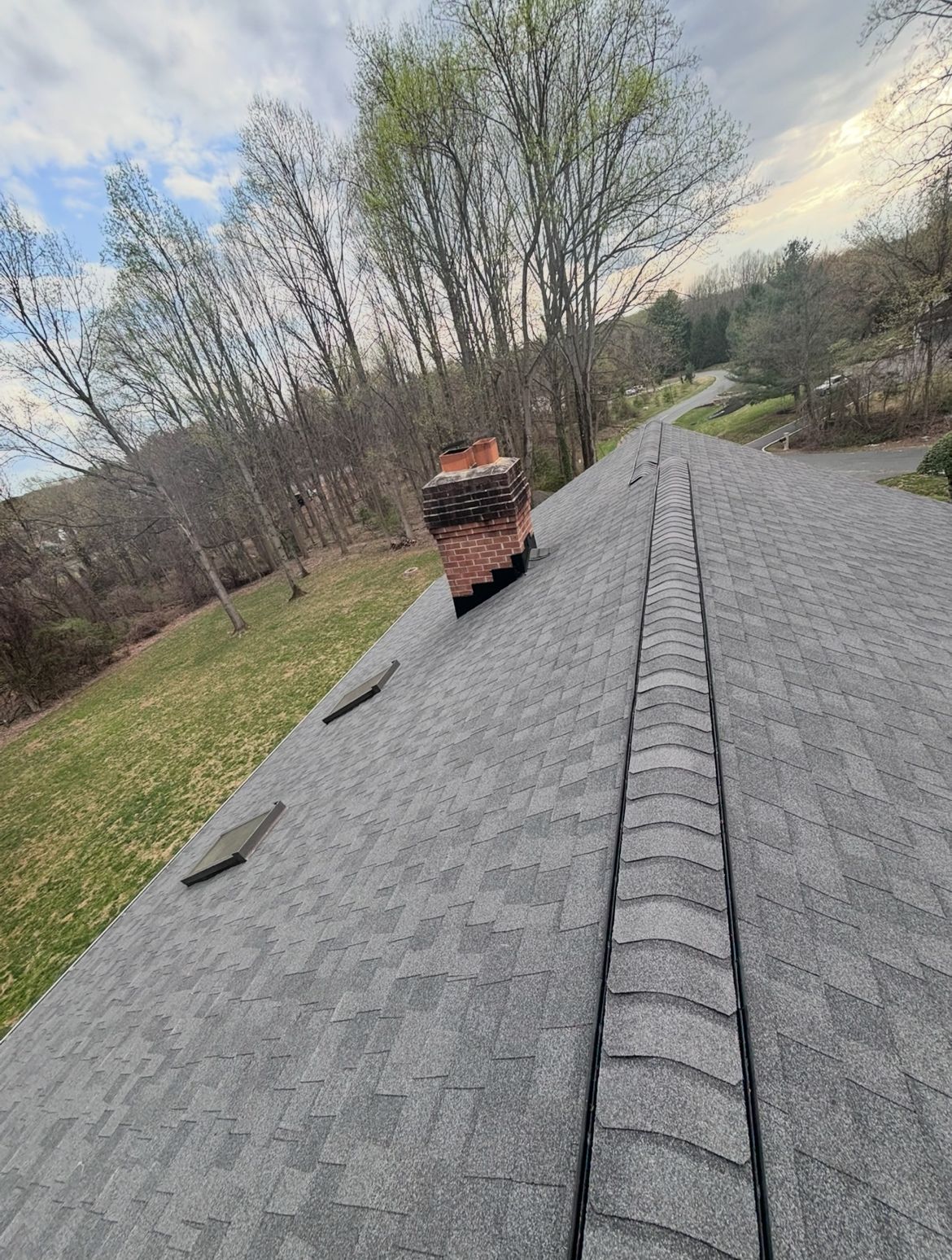 View from a roof with gray shingles, a brick chimney, and trees in the background.
