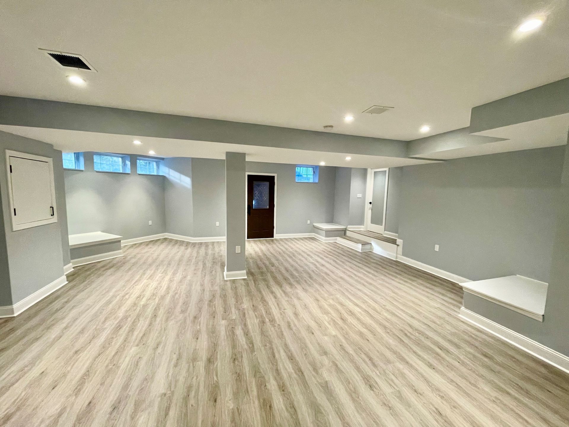 A picture of an empty basement with hardwood floors and gray walls.