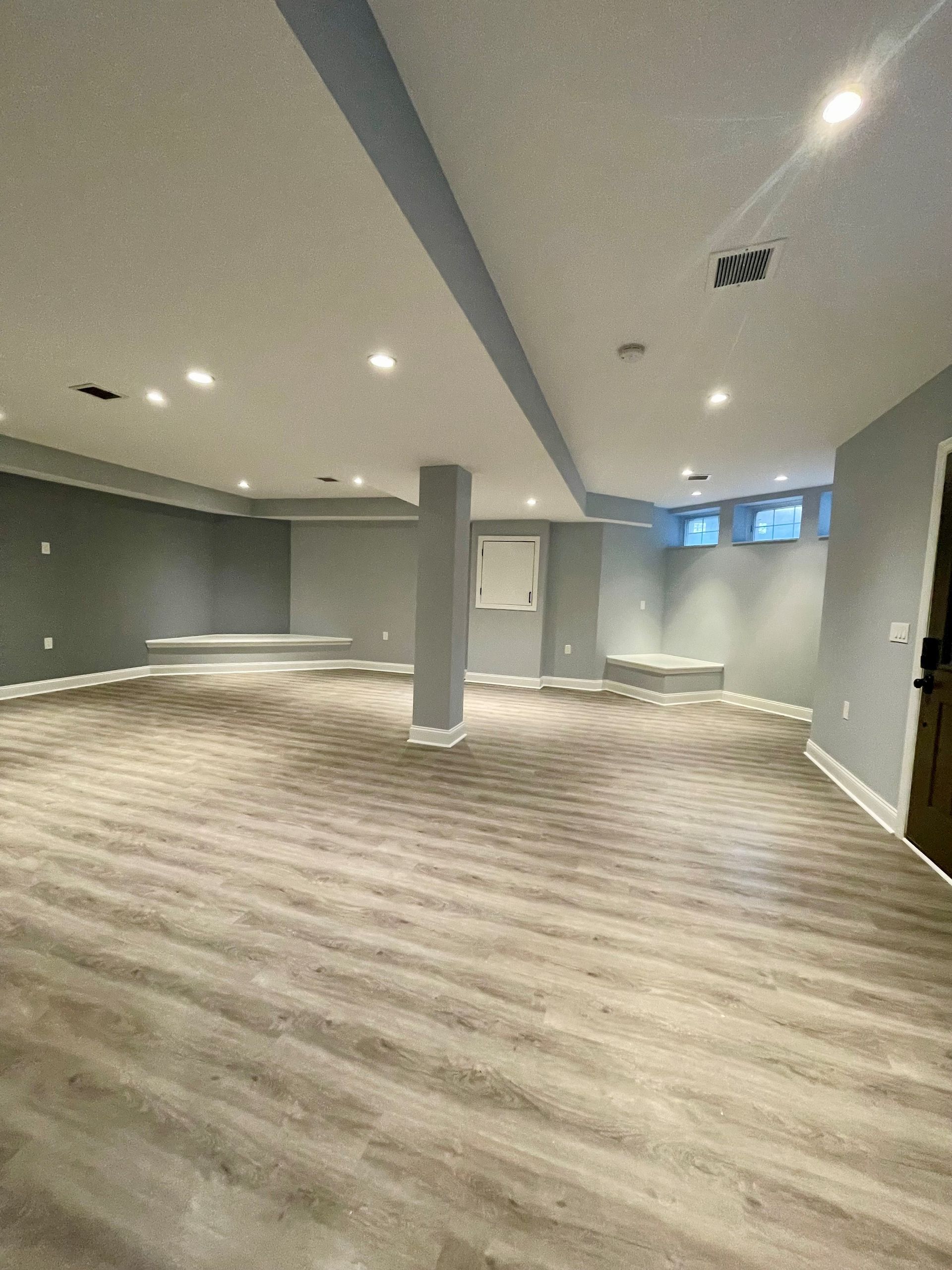 An empty basement with hardwood floors and gray walls.