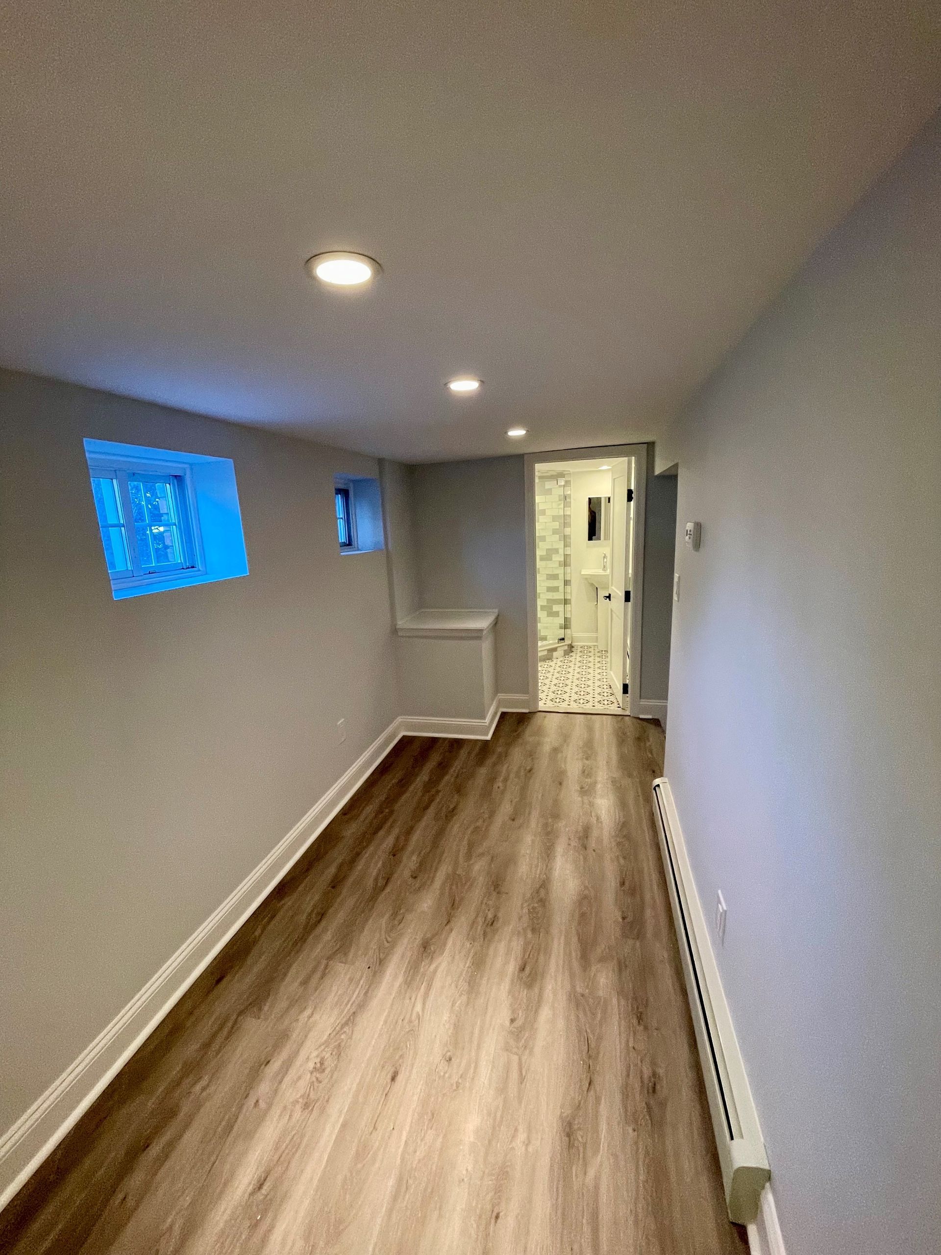 A long hallway in a basement with hardwood floors and a window.