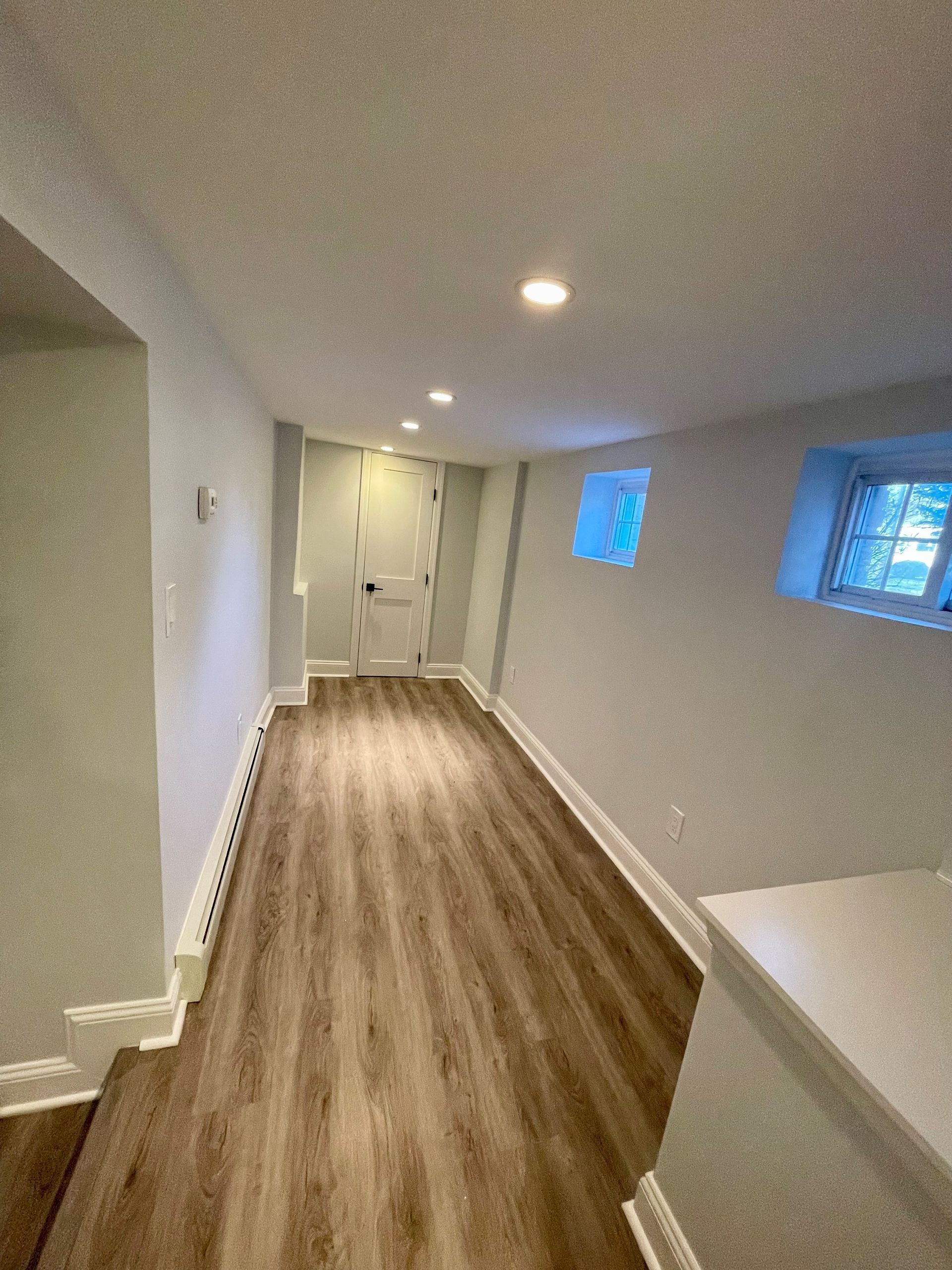 A long hallway in a basement with hardwood floors and white walls.