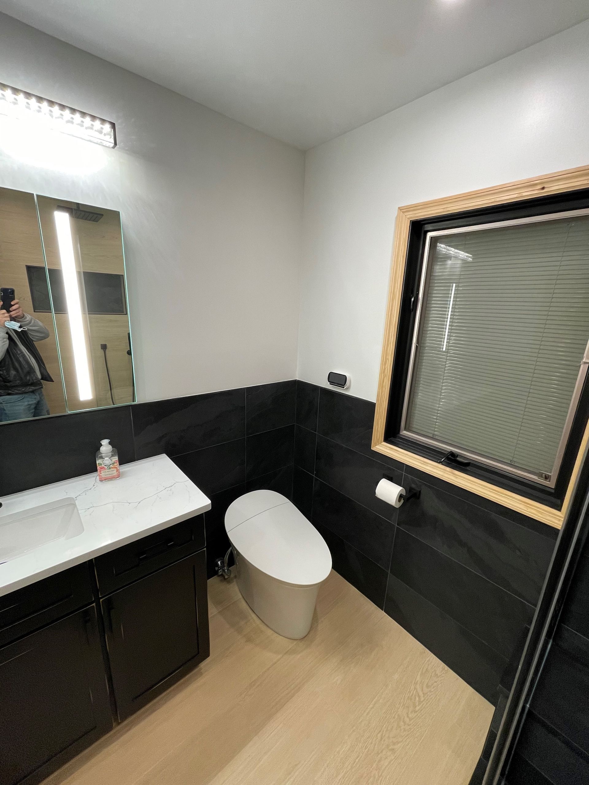 A bathroom with a toilet, sink, mirror, and window.