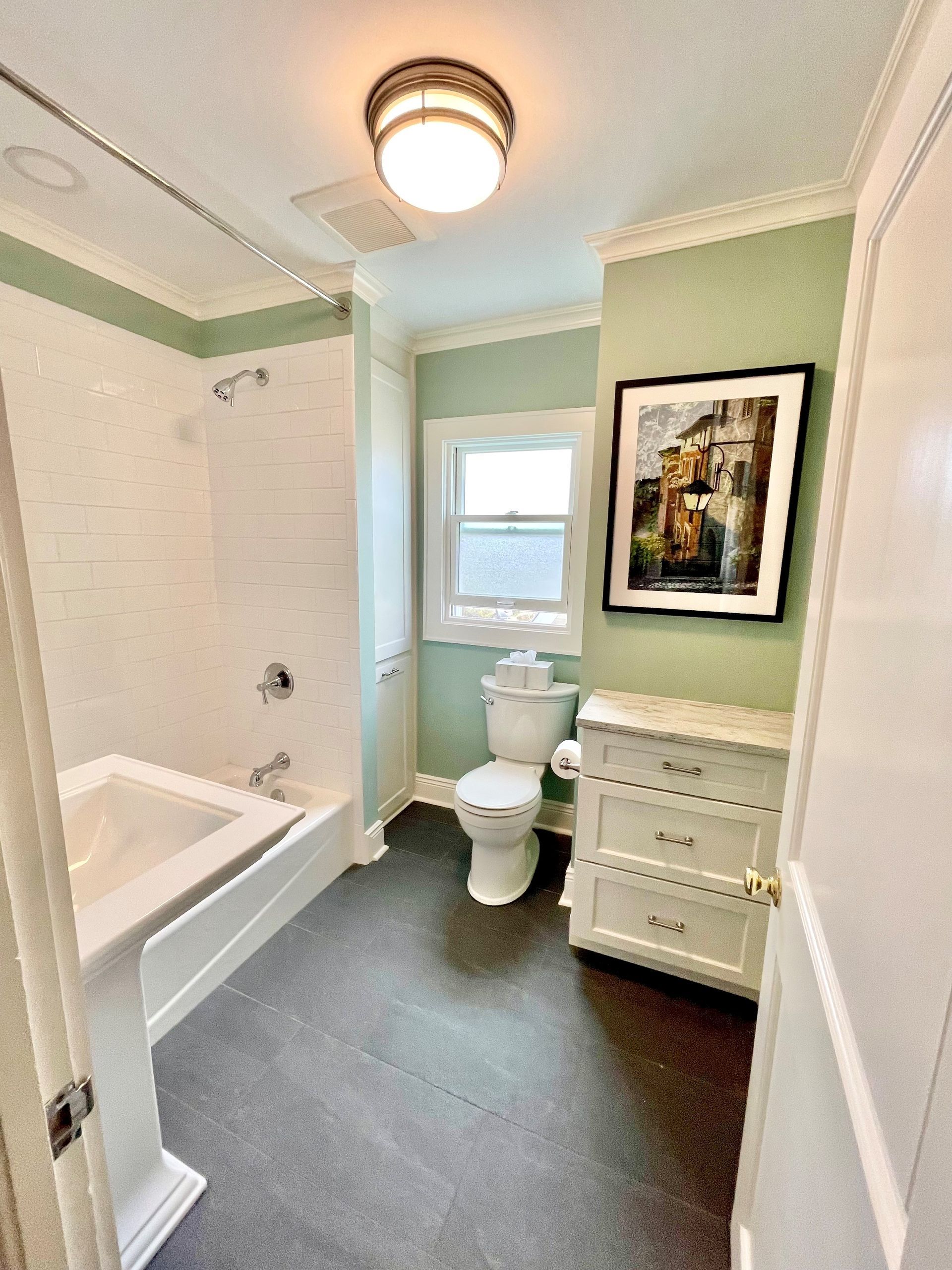 A bathroom with a toilet, bathtub, dresser, and picture on the wall.