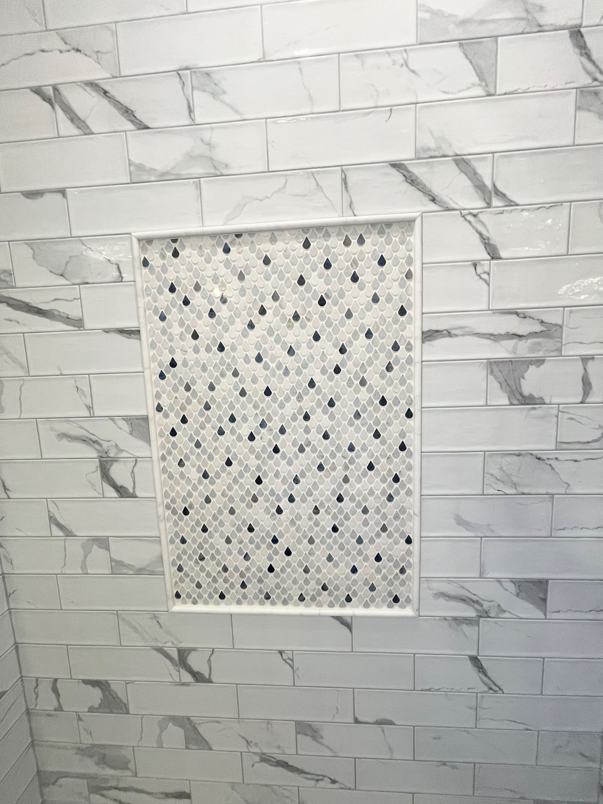 There is a shower niche in the wall with marble tiles.