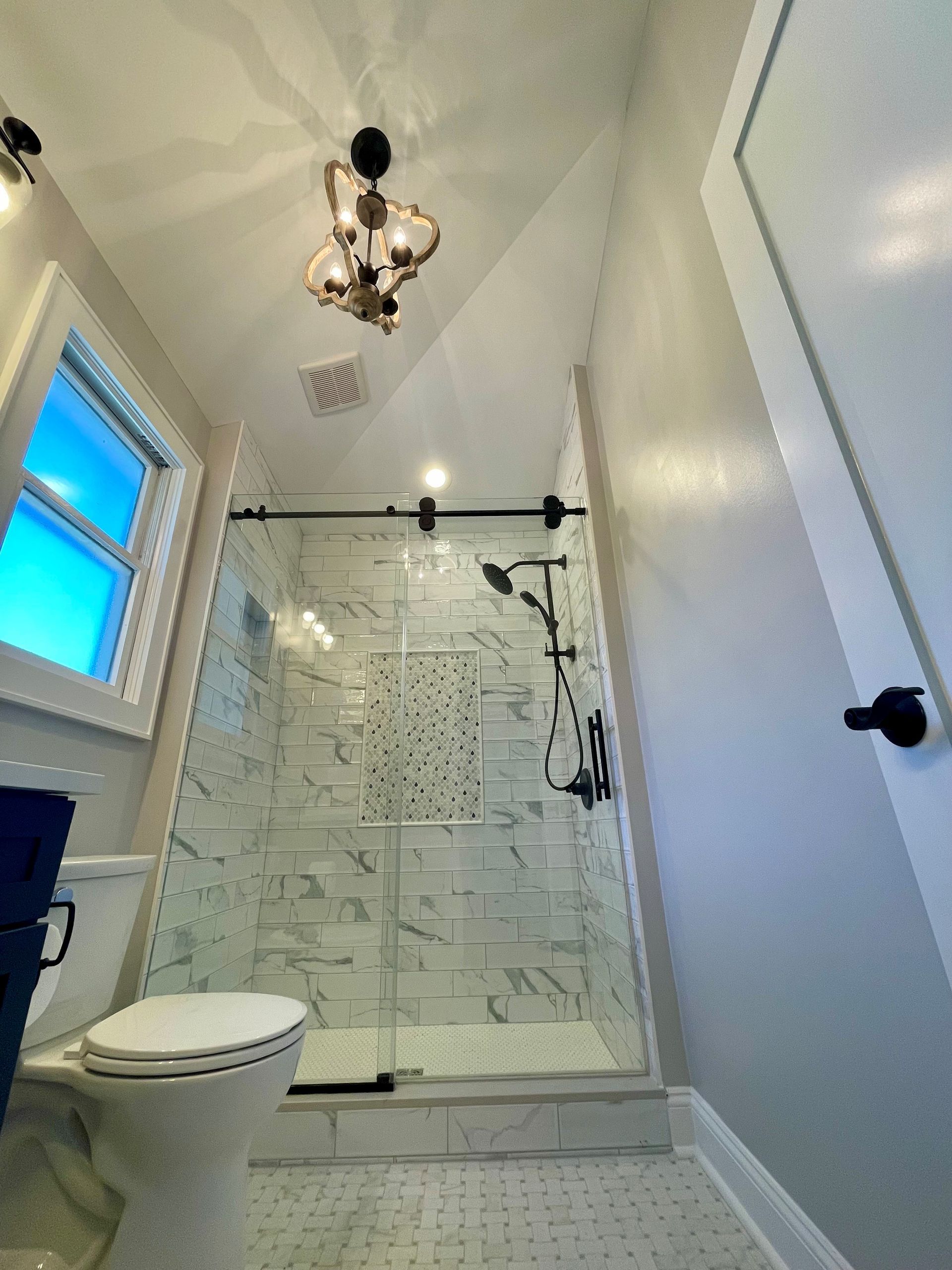 A bathroom with a toilet, shower, and window.