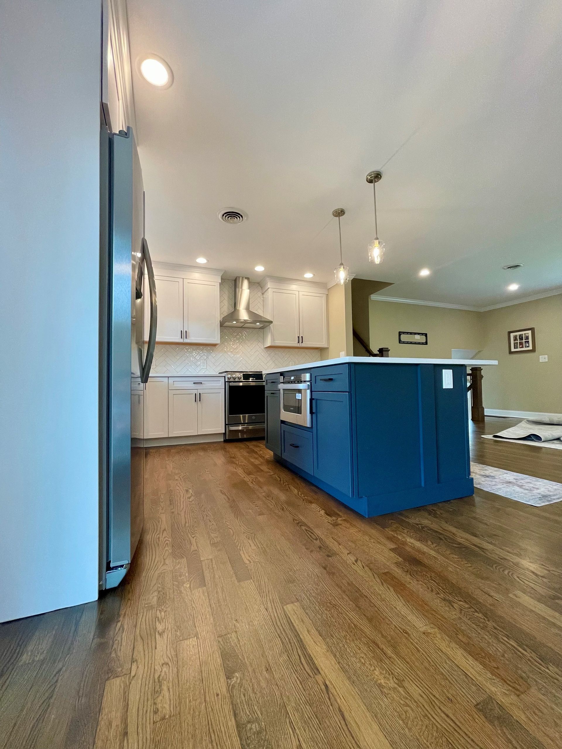 A kitchen with a blue island, white cabinets, stainless steel appliances, and hardwood floors.