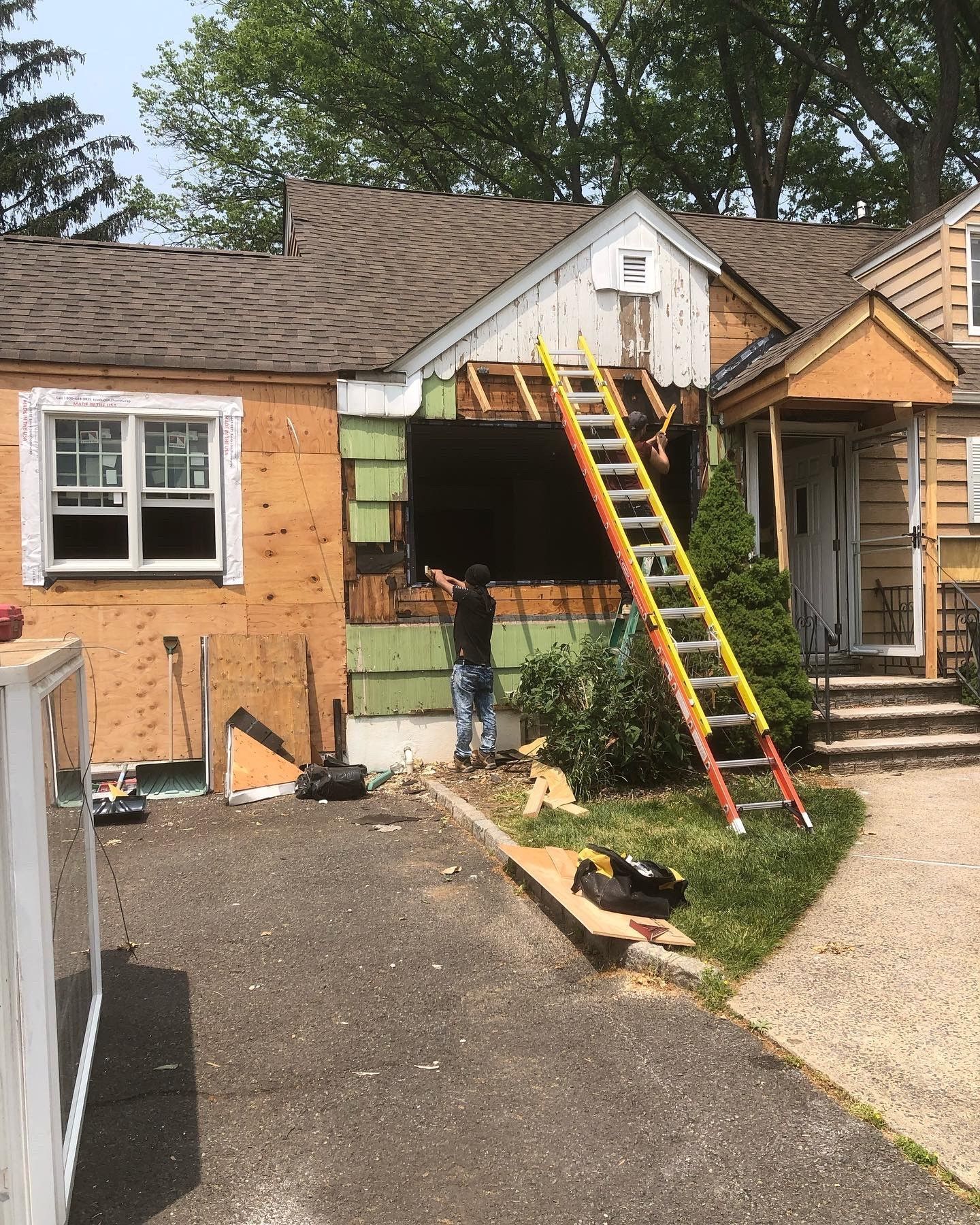 A man is standing in front of a house with a ladder.
