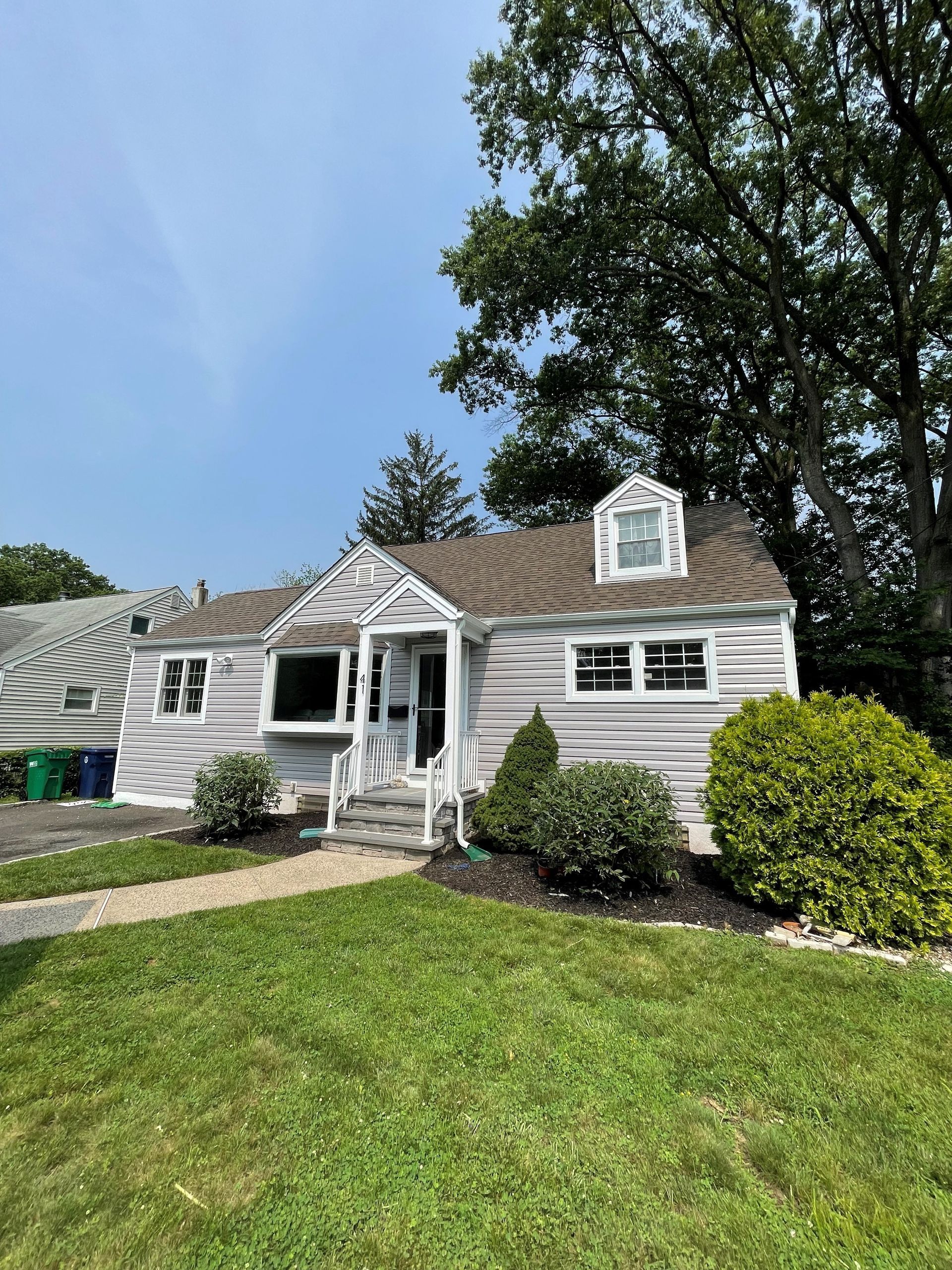 A white house with a brown roof is sitting on top of a lush green lawn.
