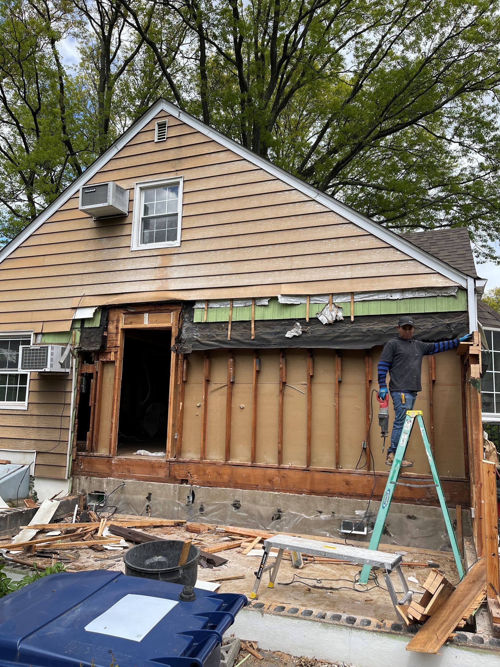 A man is standing on a ladder in front of a house that is being remodeled.
