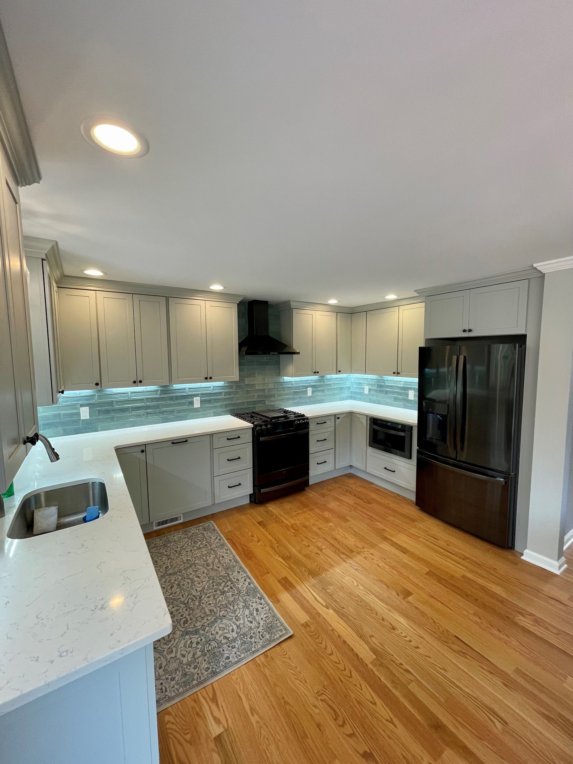 A kitchen with white cabinets, hardwood floors, a stove, refrigerator and sink.